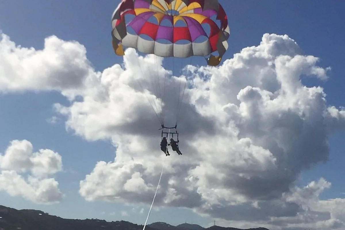Two riders gliding high above the green hills of St. Thomas while parasailing in St. Thomas USVI near Sapphire Beach